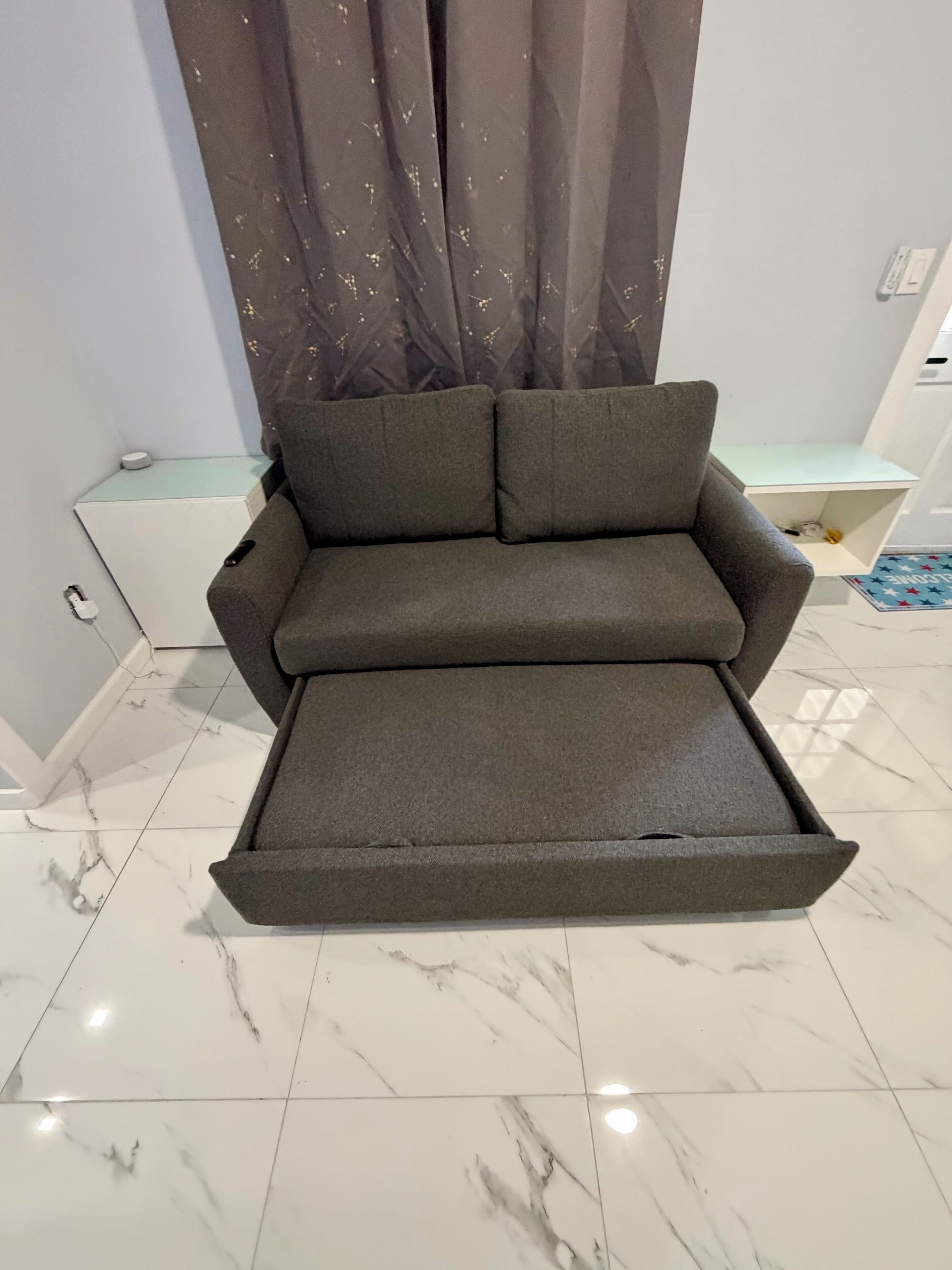 A modern room with a grey sofa, a white side table, a small white cabinet, and a tiled floor.