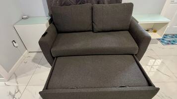 A modern room with a grey sofa, a white side table, a small white cabinet, and a tiled floor.