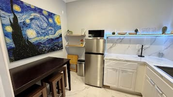Een moderne keuken met een marmeren aanrechtblad, roestvrijstalen apparatuur en een schilderij van een nachtscène aan de muur.
