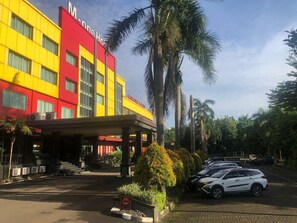 A hotel with a red and yellow facade, a covered entrance, and a parking area with cars. - M-one Hotel Bogor (Bogor)