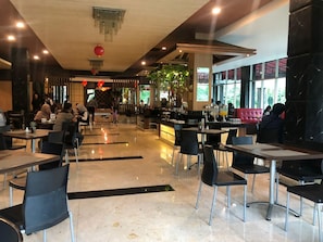 A spacious indoor dining area with tables and chairs, a bar area, and large windows providing natural light. - M-one Hotel Bogor (Bogor)