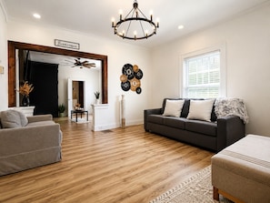 A living room with a dark grey sofa, a grey armchair, a wooden floor, a chandelier, and a wall with decorative plates.