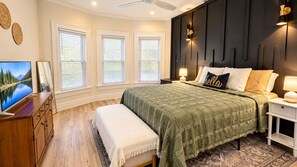Une chambre à coucher comprenant un lit, des tables de chevet, un téléviseur et une fenêtre avec des stores.