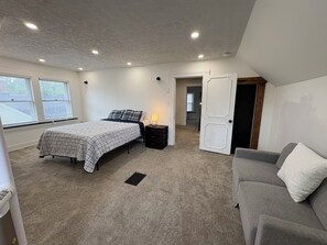 Ein Schlafzimmer mit einem Bett, einem Nachttisch, einer Lampe und einem grauen Sofa.
