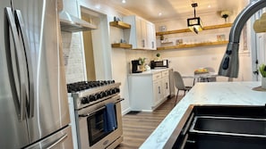 A modern kitchen with stainless steel appliances, white cabinetry, and a marble countertop.