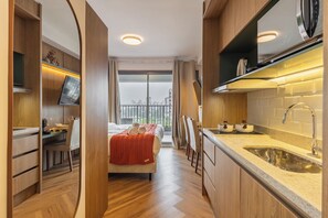 A compact hotel room with a bed, kitchenette, and a balcony with a city view. - StayHome - Moema Cyrela - Piscina & Gym (São Paulo)
