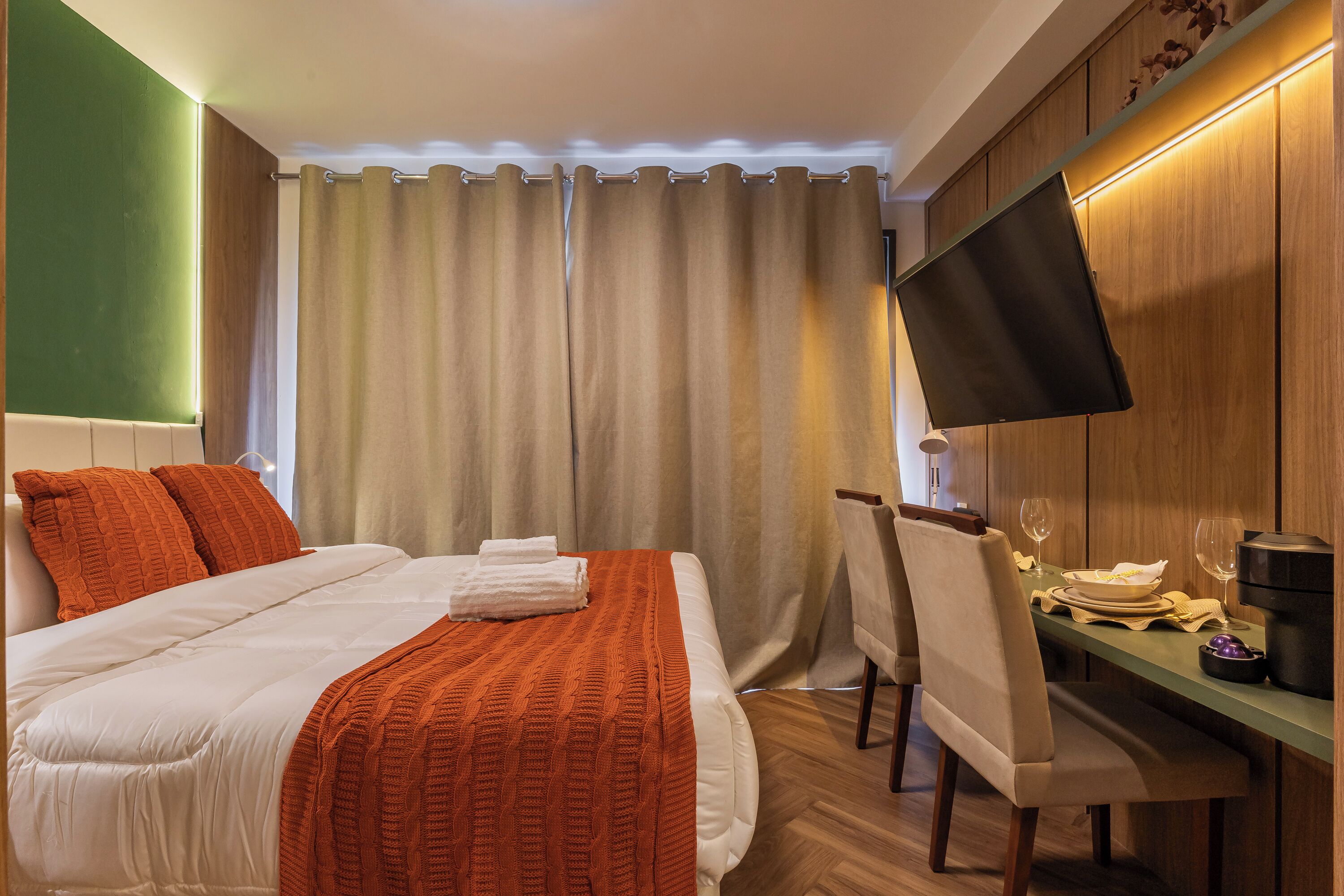 Une chambre d’hôtel comprenant un lit, un bureau avec une chaise, un téléviseur à écran plat et une table à manger dressée pour deux personnes.