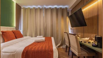 A hotel room with a bed, a desk with a chair, a flat-screen TV, and a dining table set for two.