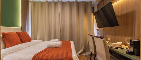 A hotel room with a bed, a desk with a chair, a flat-screen TV, and a dining table set for two.