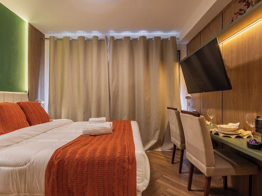 Habitación de hotel con cama, escritorio con silla, televisor de pantalla plana y mesa de comedor para dos.
