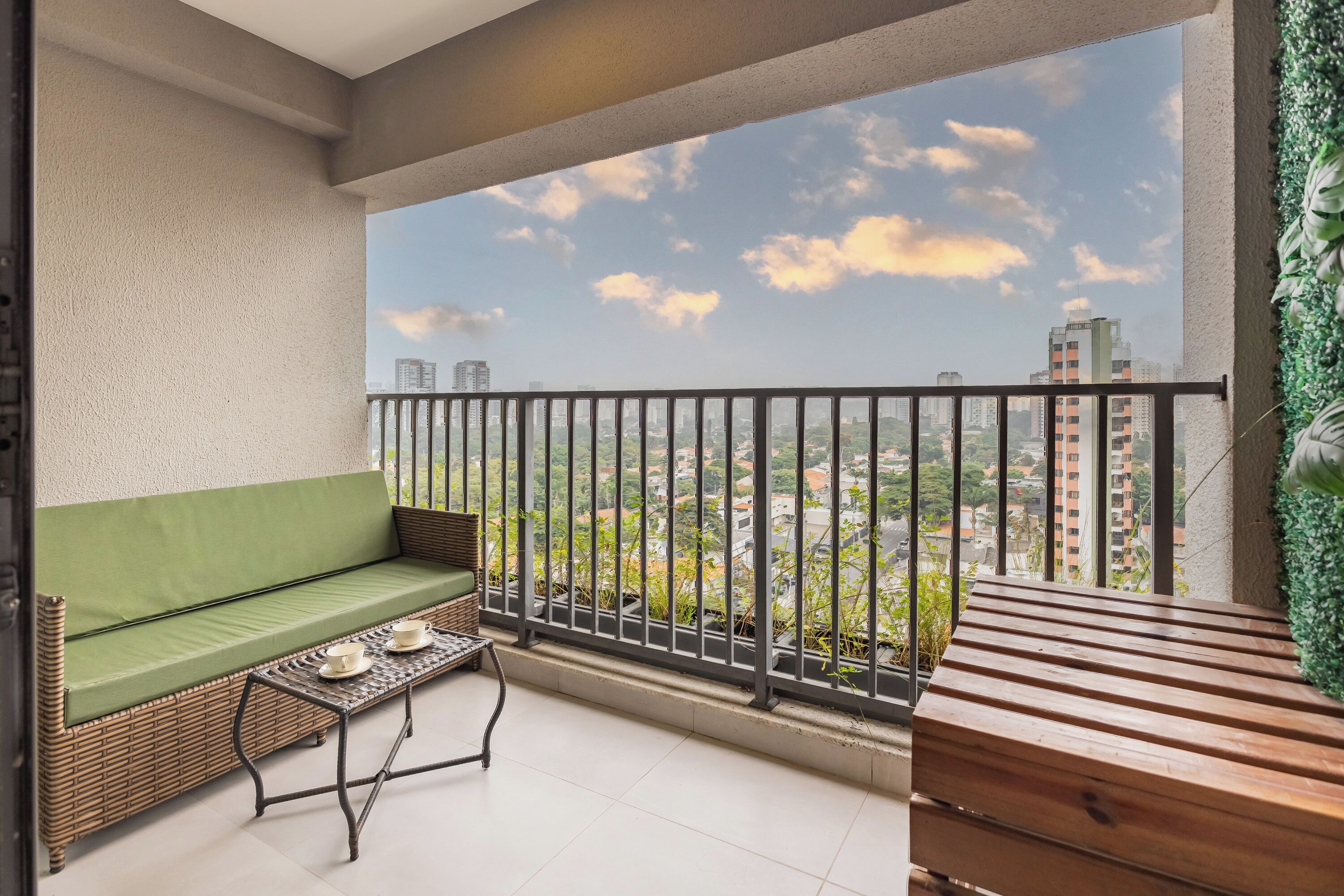 A balcony with a green sofa, a small table with cups, and a wooden bench.