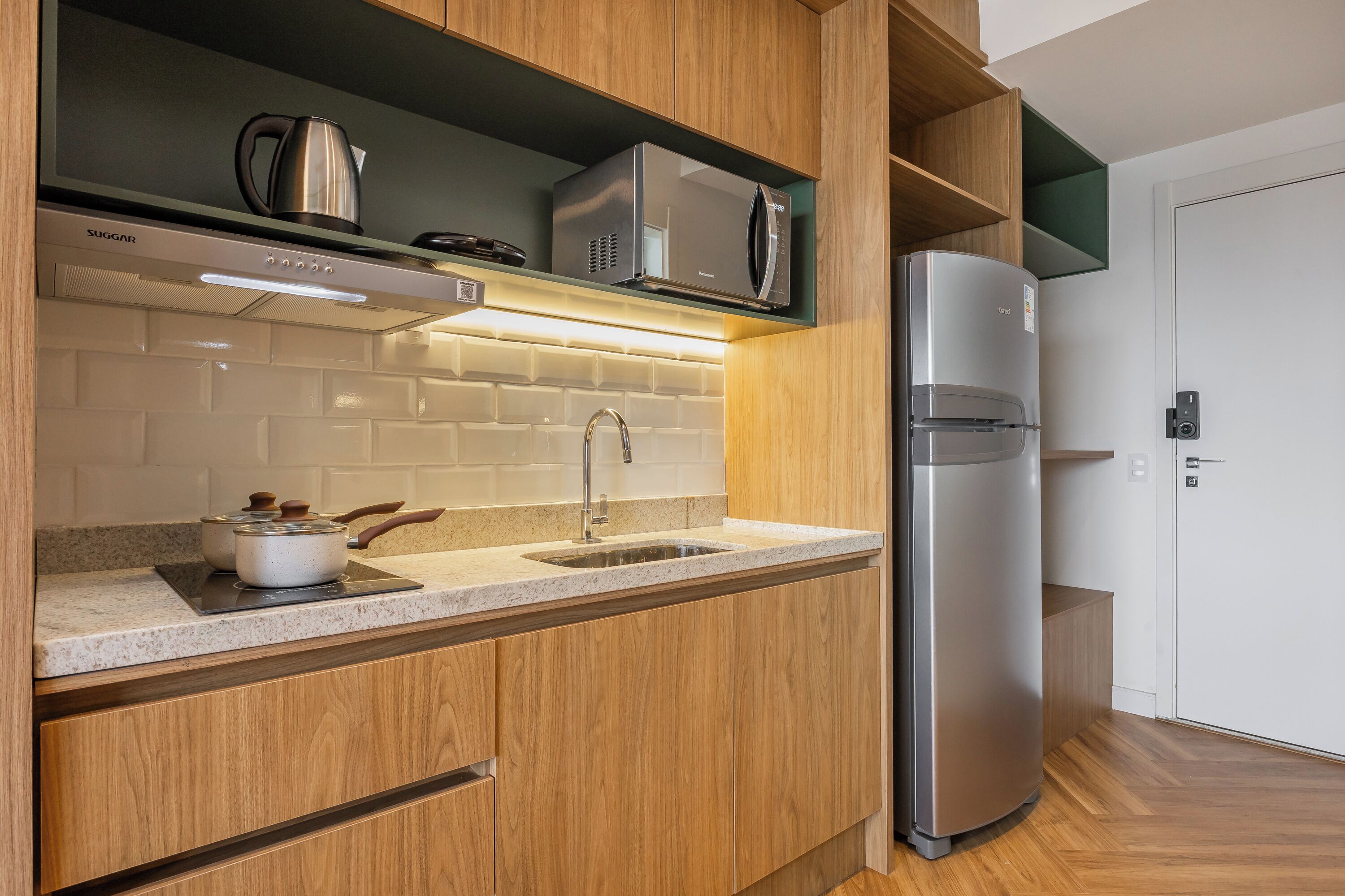 A modern kitchen with wooden cabinets, a stainless steel refrigerator, a microwave, and a kettle.