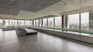 Una habitación amplia con un banco largo, ventanas grandes y vista a la ciudad.