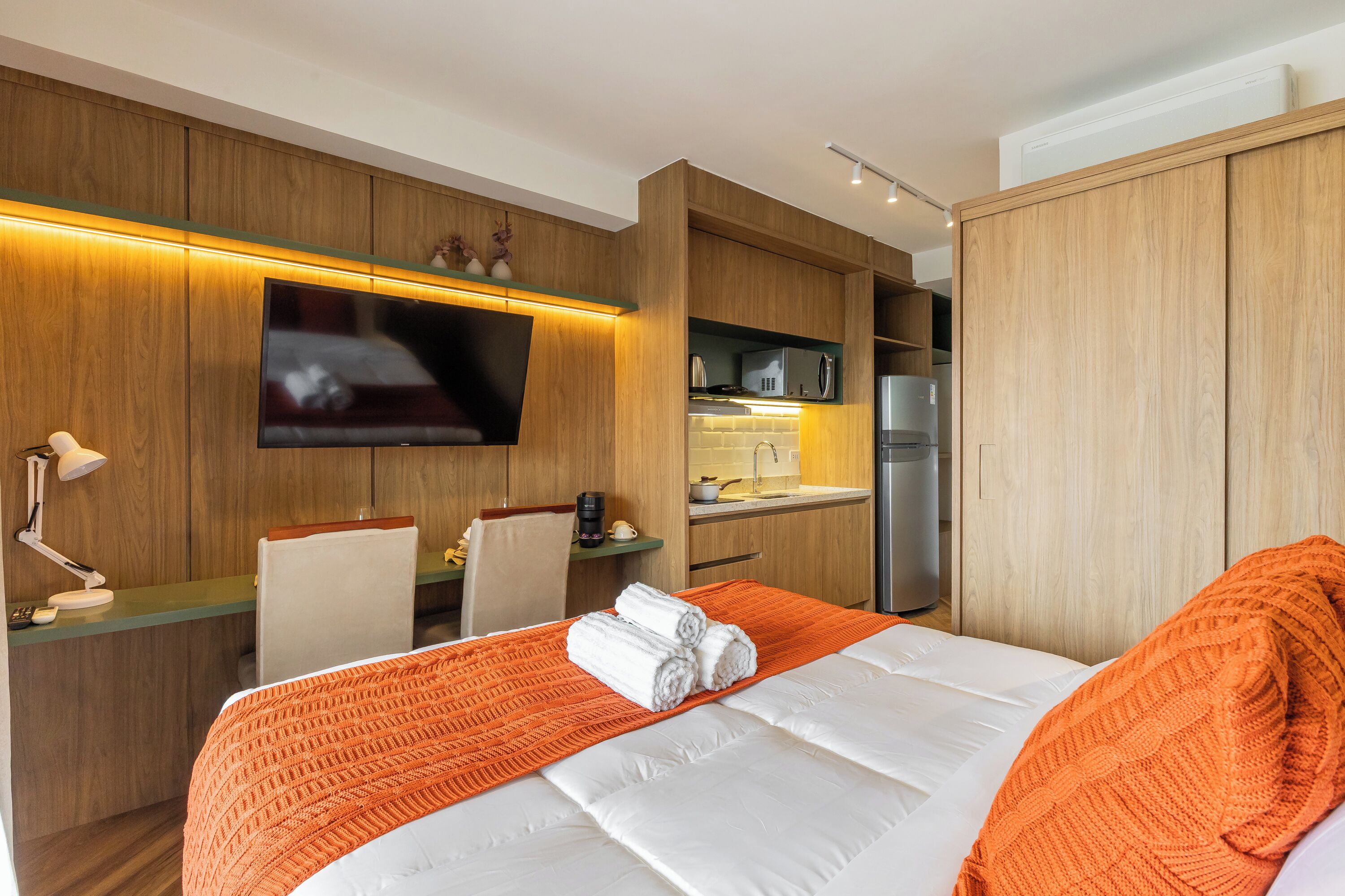 Quarto de hotel com cama, escrivaninha, televisão, micro-ondas e frigorífico.