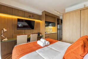 A hotel room with a bed, a desk, a television, a microwave, and a refrigerator. - StayHome - Moema Cyrela - Piscina & Gym (São Paulo)