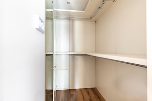 A modern, empty walk-in closet with glass doors, wooden flooring, and metal shelving units. - Stylish Bayswater Apartment near Hyde Park (London)