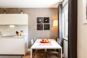 A modern kitchen with white cabinets, a dining table with chairs, and a fruit bowl. - Stylish Bayswater Apartment near Hyde Park (London)