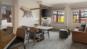 A modern living room with a stone fireplace, a dining area with a granite table, and a large window offering a view of buildings. - 1 Bedroom Villa Timber Lodge Resort S Lake Tahoe (South Lake Tahoe)
