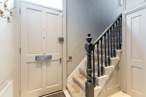 A staircase with a black balustrade leading to a landing, white doors on either side, and a metal doorknob on the left door. - Elegant Four-Bed Fulham Home (London)