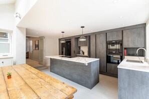 A modern kitchen with a central island, built-in appliances, and pendant lighting. - Elegant Four-Bed Fulham Home (London)