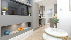 Eine moderne Küche mit eingebauten Geräten, einem an der Wand befestigten Fernseher und einer Essecke mit weißem Tisch und goldenen Beinen.