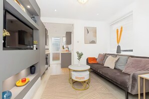 Een moderne woonkamer met een bank, een rond bijzettafeltje en een flatscreen televisie aan de muur.