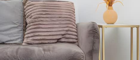 A grey sofa with a textured cushion and a vase with dried plants on a small table beside it.