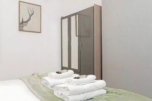 A hotel room with a bed, a wardrobe, and a framed deer head artwork. - Modern London Apartment for Business Stays (Greater London)