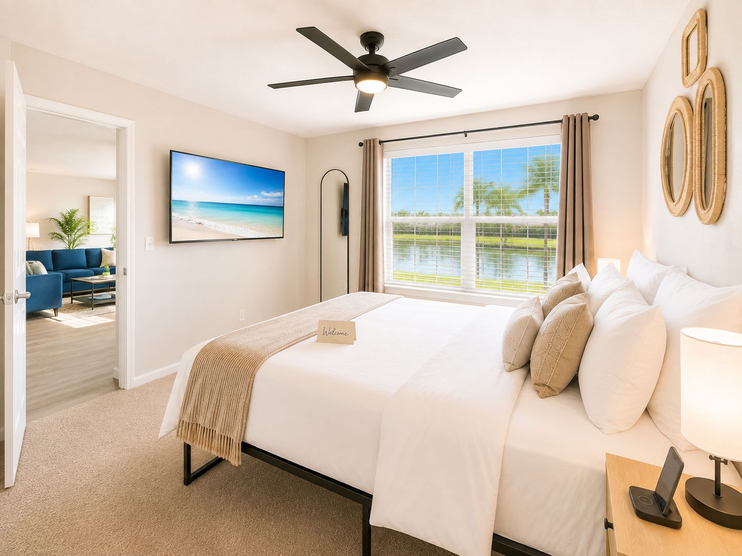 A hotel room with a bed, a ceiling fan, a window with a view of a lake, and a painting on the wall.