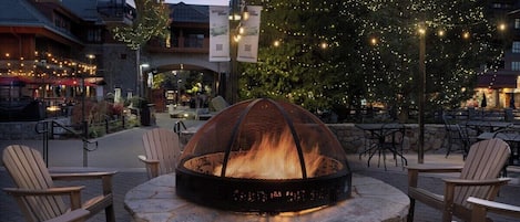 An outdoor seating area with Adirondack chairs and a stone fire pit.
