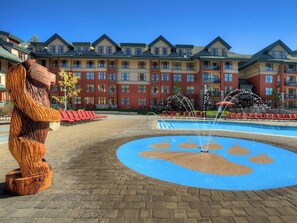 Ein Hotel mit einem großen Brunnen, einer Holzbär-Skulptur und einem Pool mit Pfotenabdruck-Design.