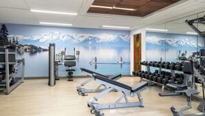 Un gimnasio con equipo de ejercicio, un espejo grande y un mural que muestra un lago y montañas.