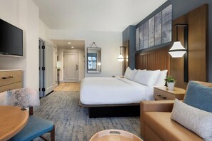 Quarto de hotel com cama, escrivaninha, cadeira, televisão e obra de arte na parede.