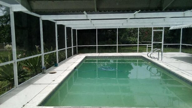 A rectangular pool with a white deck and a covered area with a metal roof. - Spacious 3-bedroom house in Fort Myers with pool, straight drive to the beach (Fort Myers)