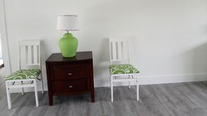 A room with a white wall, a green vase on a wooden nightstand, two white chairs with green patterned cushions, and a grey carpet. - Spacious 3-bedroom house in Fort Myers with pool, straight drive to the beach (Fort Myers)