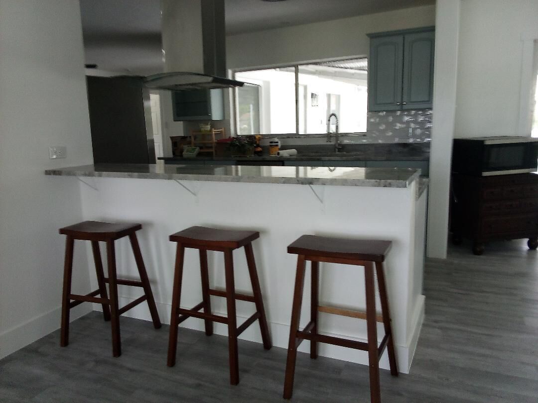 A kitchen with a central island, three wooden stools, and a dark wood cabinet.
