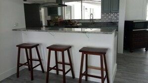 A kitchen with a central island, three wooden stools, and a dark wood cabinet. - Spacious 3-bedroom house in Fort Myers with pool, straight drive to the beach (Fort Myers)