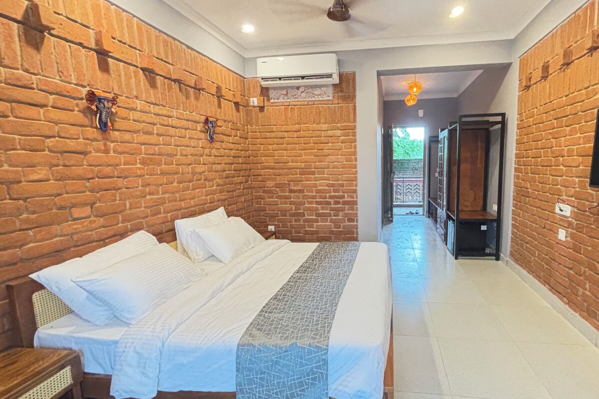 A hotel room with a brick wall, a bed with white bedding, a flat-screen TV, and an air conditioning unit.