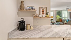 A kitchen with marble countertops, a coffee maker, a vase, and a shelf with decorative items. - Tangerine Tides: Resort Pool/Spa, On Beach, Lanai (Fort Myers Beach)
