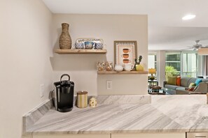A kitchen with marble countertops, a coffee maker, a vase, and a shelf with decorative items. - Tangerine Tides: Resort Pool/Spa, On Beach, Lanai (Fort Myers Beach)