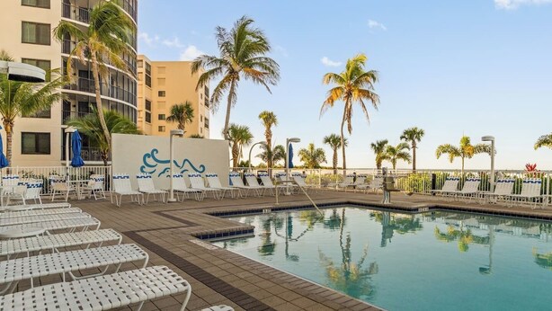 A pool area with lounge chairs, palm trees, and a building in the background. - Tangerine Tides: Resort Pool/Spa, On Beach, Lanai (Fort Myers Beach)