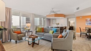 A modern living room with a sofa, armchairs, a glass coffee table, and a dining area with chairs. - Tangerine Tides: Resort Pool/Spa, On Beach, Lanai (Fort Myers Beach)
