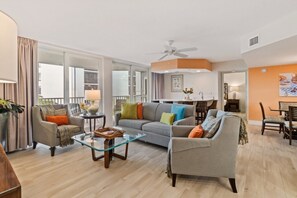 A modern living room with a sofa, armchairs, a glass coffee table, and a dining area with chairs. - Tangerine Tides: Resort Pool/Spa, On Beach, Lanai (Fort Myers Beach)