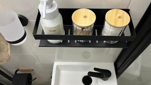 Un baño con un lavamanos blanco, un dispensador de jabón negro y dos recipientes con tapas de madera.