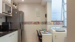A compact kitchen with a refrigerator, microwave, and washing machine, a small dining table, and a window providing natural light. - 9 min From Copacabana Beach Ml905 (Rio de Janeiro)