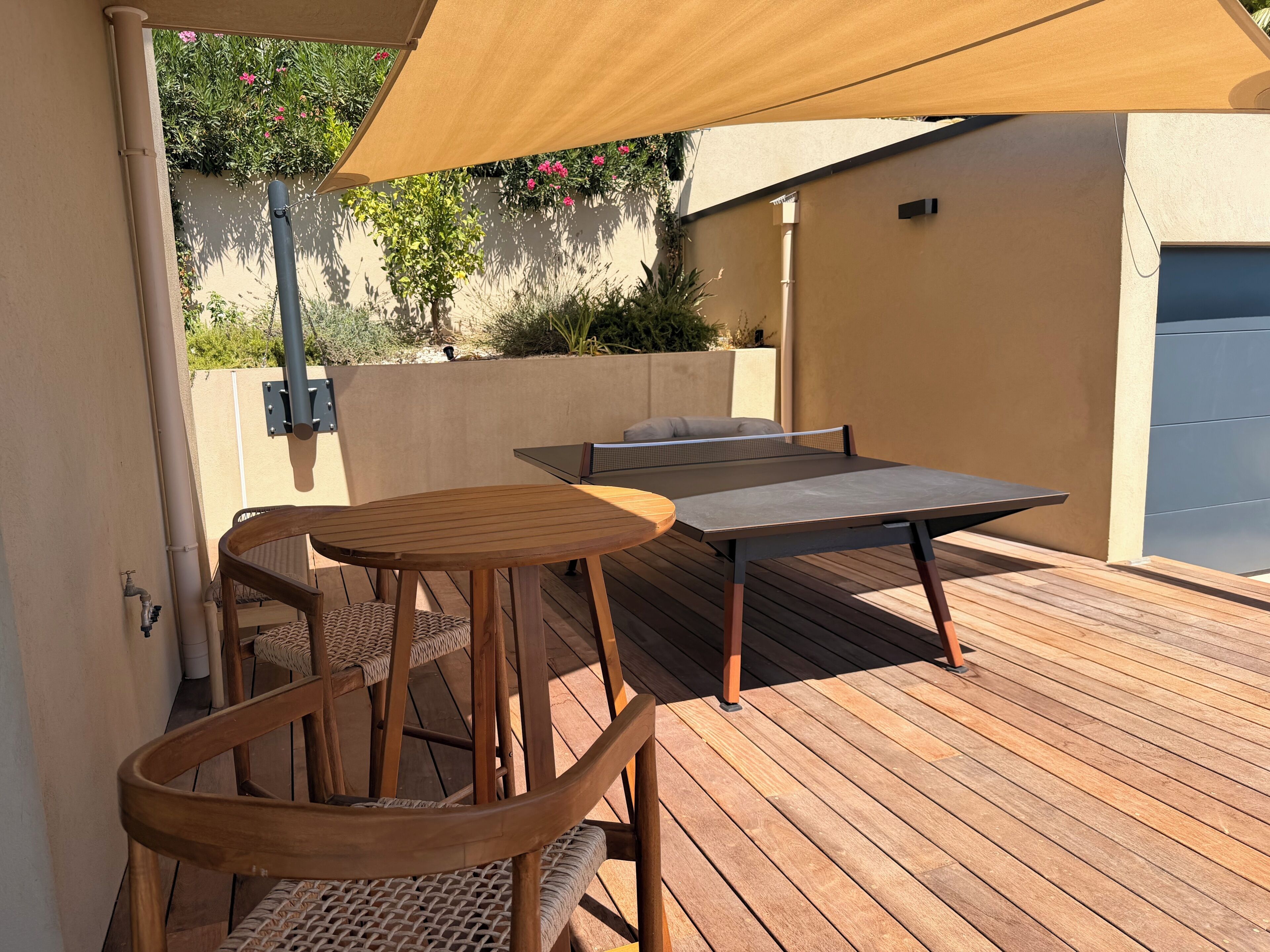Una terrazza esterna con tavolo e sedie, un tavolo da ping pong e un pergolato che offre ombra.