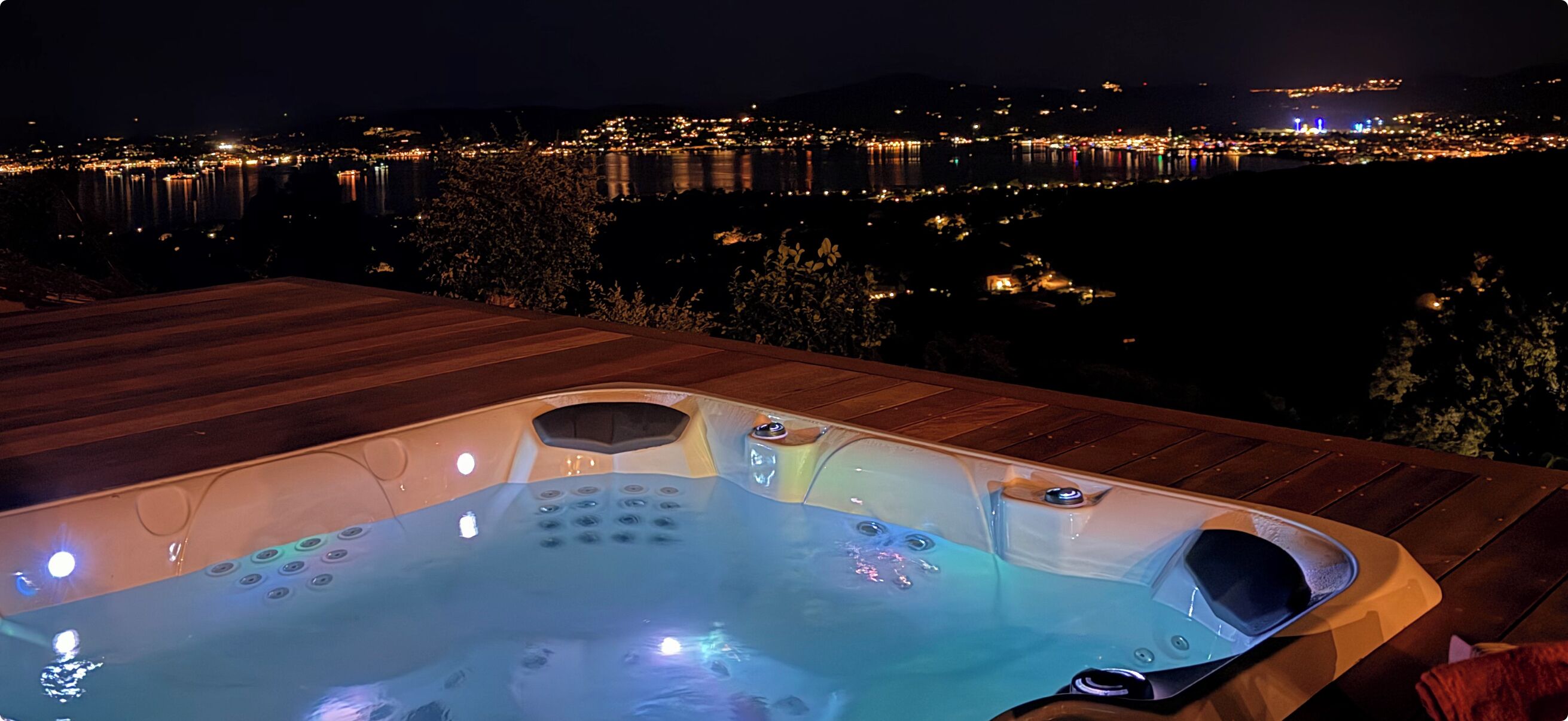 A hot tub on a wooden deck with a cityscape view at night.