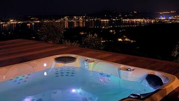 A hot tub on a wooden deck with a cityscape view at night.