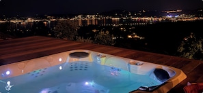 Un bain à remous sur une terrasse en bois, avec vue sur la ville illuminée la nuit.
