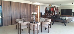 A modern living room with a glass dining table surrounded by chairs, a sofa, and a TV.